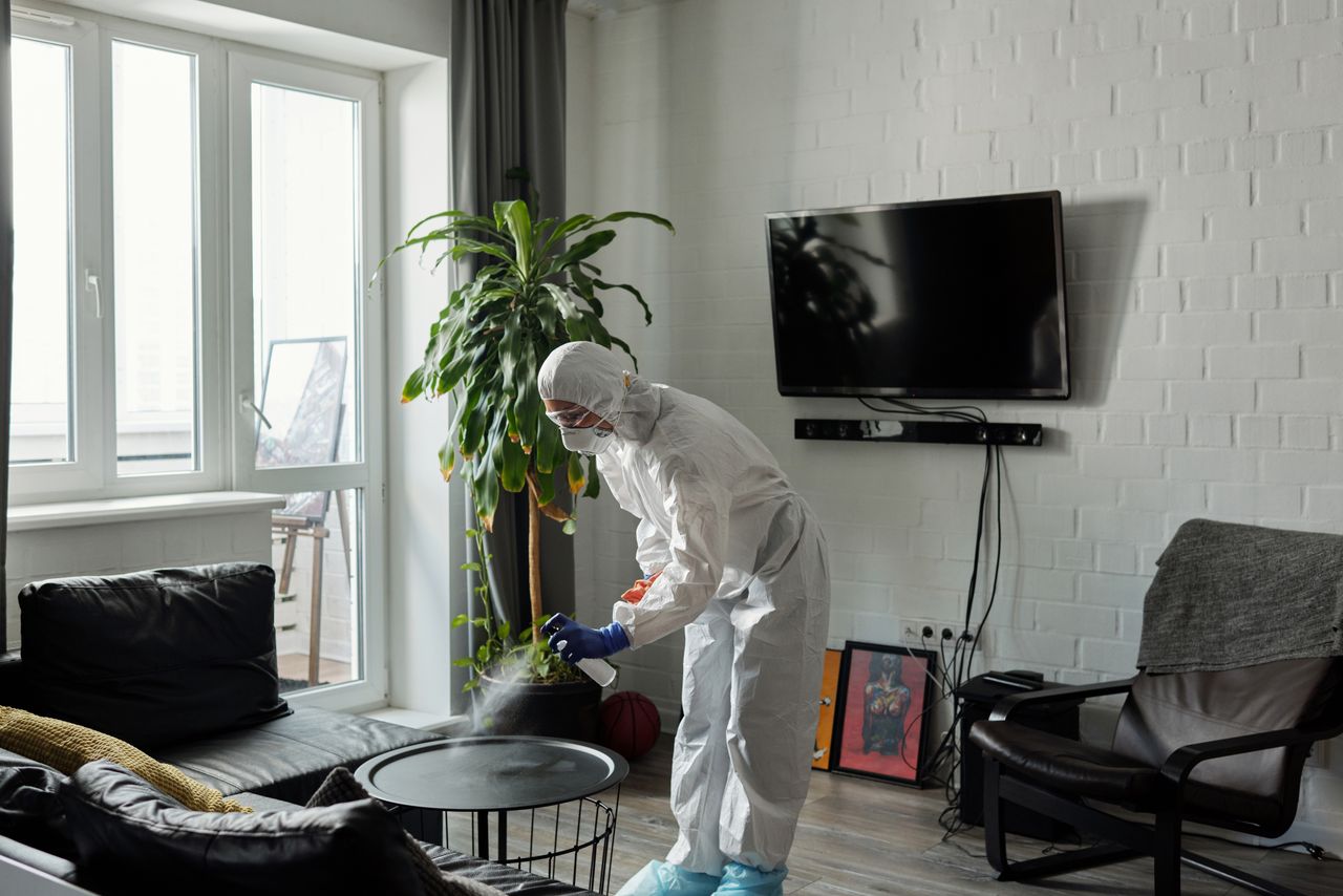 creative Worker in PPE disinfecting a living room, ensuring safety from viruses.