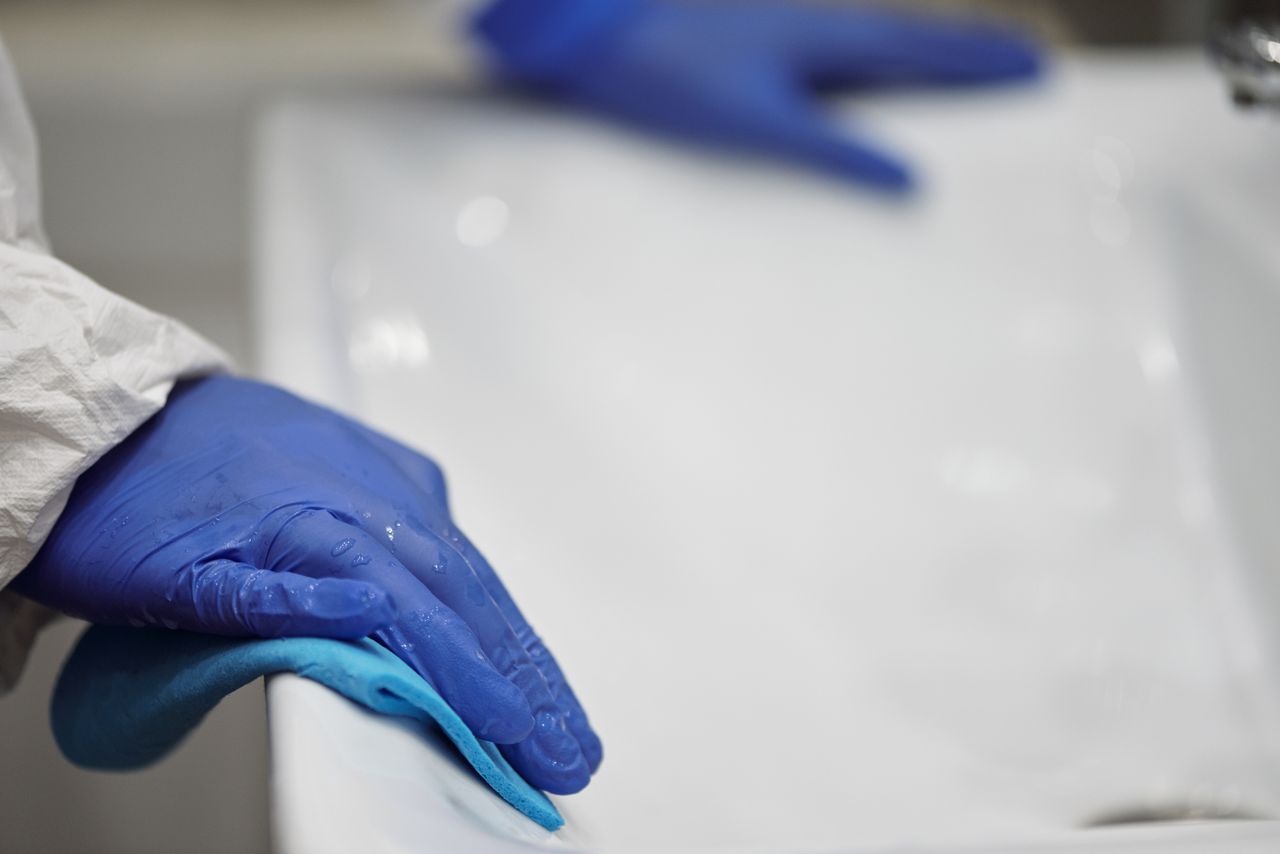 Services-01 Close-up of a person sanitizing a bathroom sink with gloves and cloth, focusing on hygiene and cleanliness.