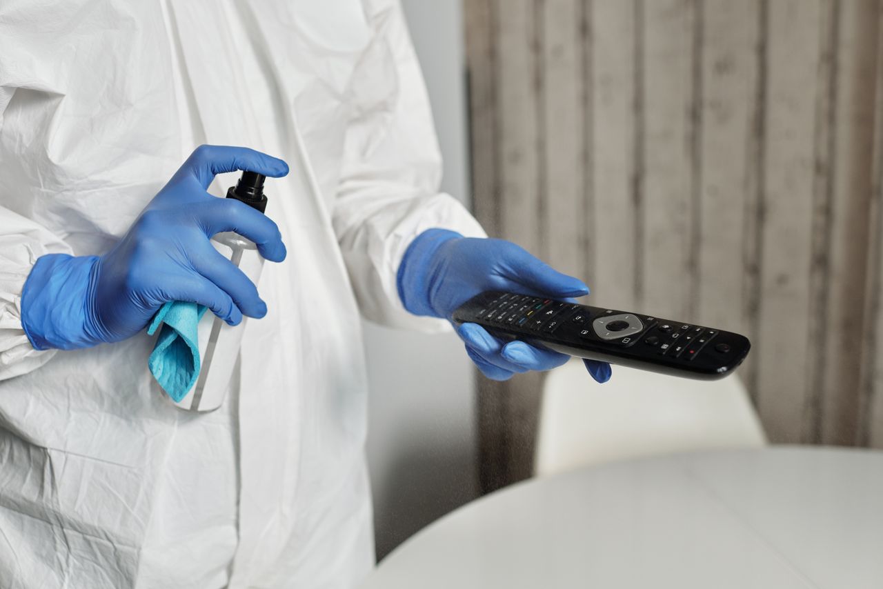 Services-02 Hands in gloves disinfecting a remote control indoors. Pandemic hygiene concept.